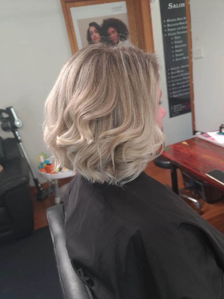 A shoulder-length blonde layered bob with soft waves and bright creamy highlights.