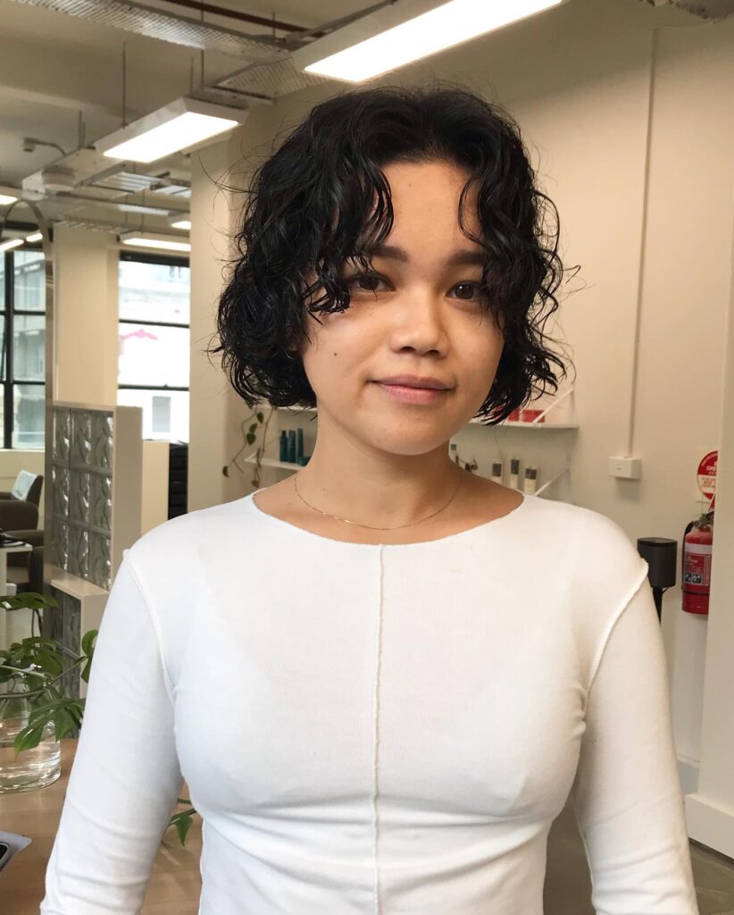 Short dark curly bob with layered waves and soft curtain fringe pieces.