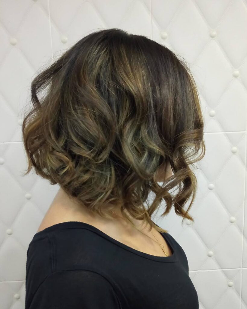 Medium brown layered bob with soft curled waves and subtle caramel highlights.