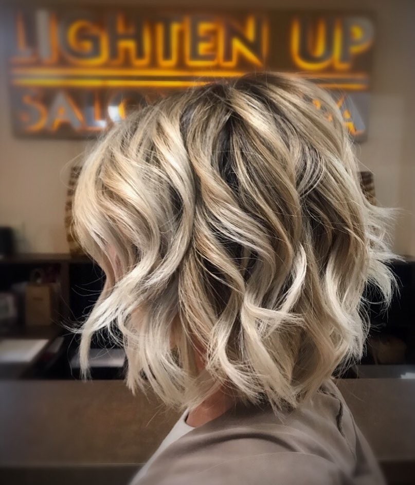 Layered blonde bob with dark roots and loose textured waves.