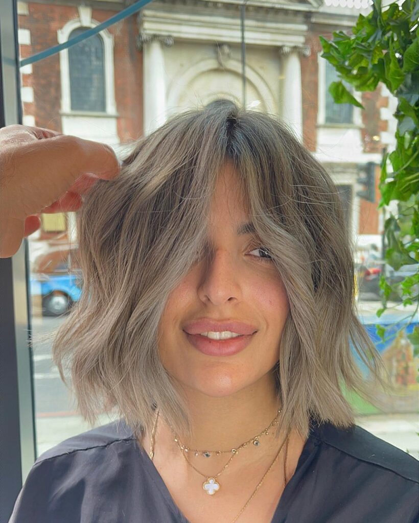 Wavy ash blonde layered bob with soft curtain pieces and smoky cool toned dimension.