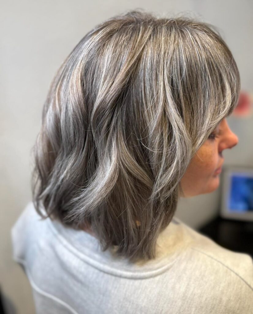 Dimensional ash blonde layered lob with soft waves and blended cool-toned highlights.