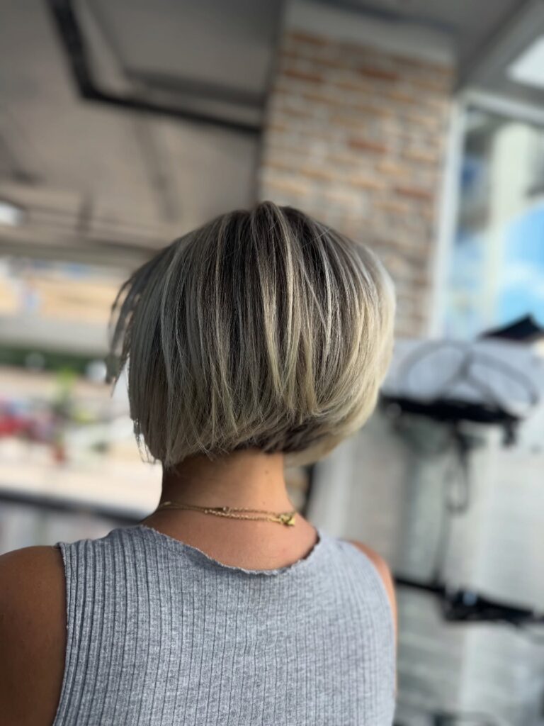 A blunt ash-blonde layered bob with darker roots, a sleek rounded shape, and soft stacked volume in the back.