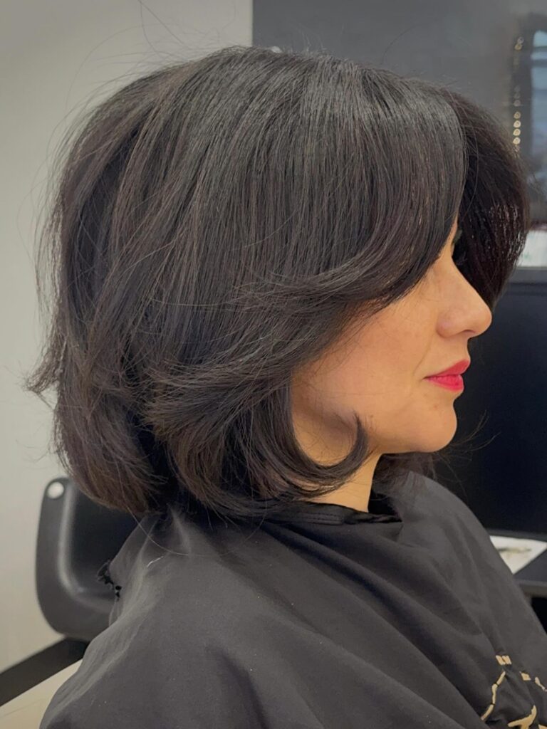Dark espresso layered bob with side swept bangs and soft rounded volume near the jawline.