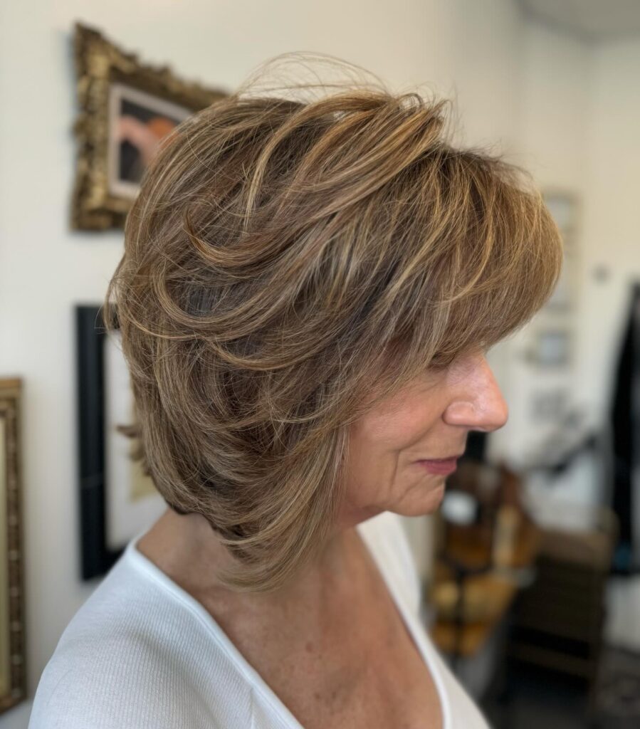 Feathered caramel brown layered bob with side-swept bangs and voluminous stacked layers.