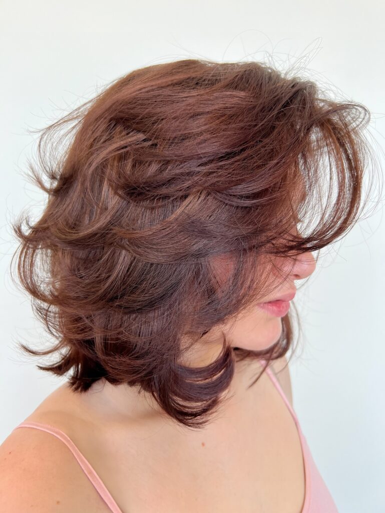 Shaggy chocolate brown layered bob with wispy bangs and flipped textured ends.
