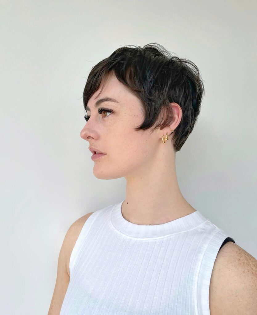 A woman with thick dark brown hair in a tapered pixie cut with soft side-swept bangs and delicate layers around the ears.