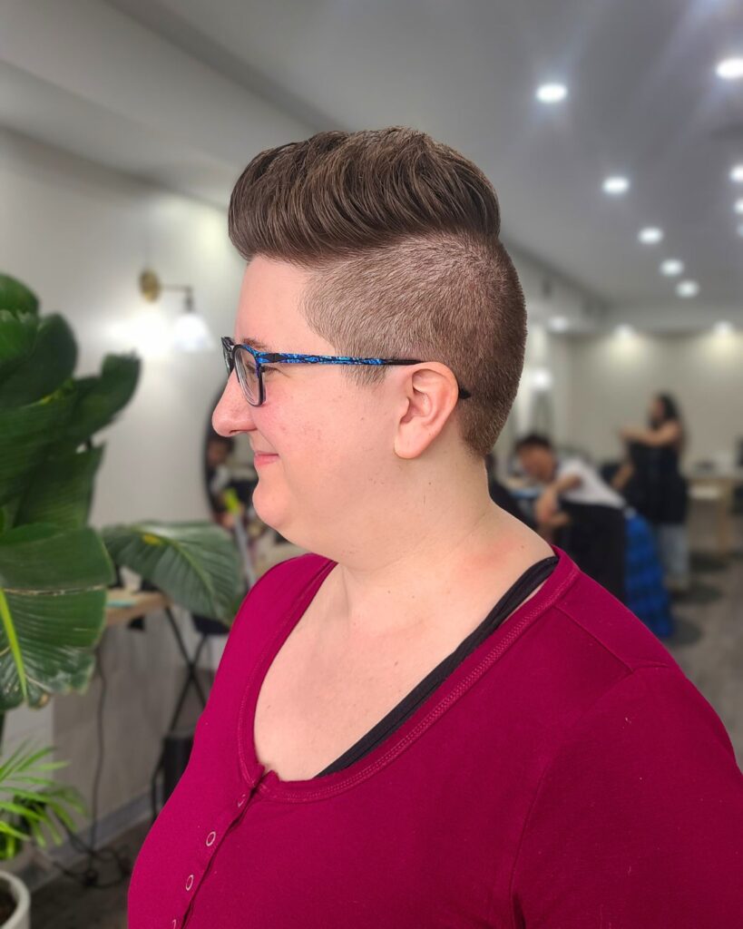 A woman with thick brown hair styled in a high pompadour with closely shaved sides and back.