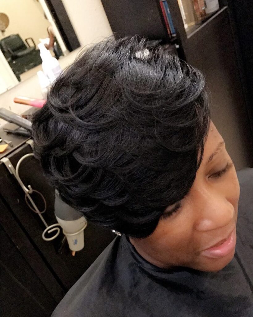 A woman with thick jet-black hair styled in a layered pixie cut with sculpted voluminous waves and a side-swept fringe.