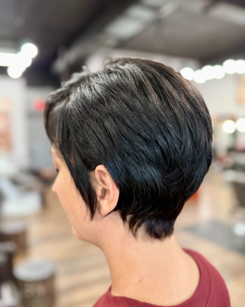 A woman with thick, glossy black hair styled in a layered pixie cut with a tapered nape and soft wispy pieces around the ears.