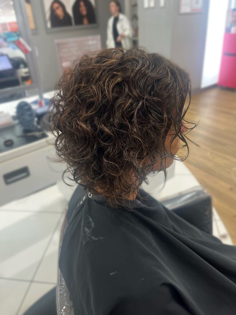 Layered curly bob with defined soft coils and caramel highlights styled with natural volume.