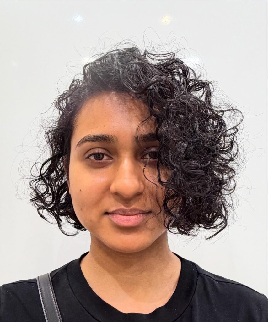 Asymmetrical layered curly bob with soft side-swept coils and dark natural texture.