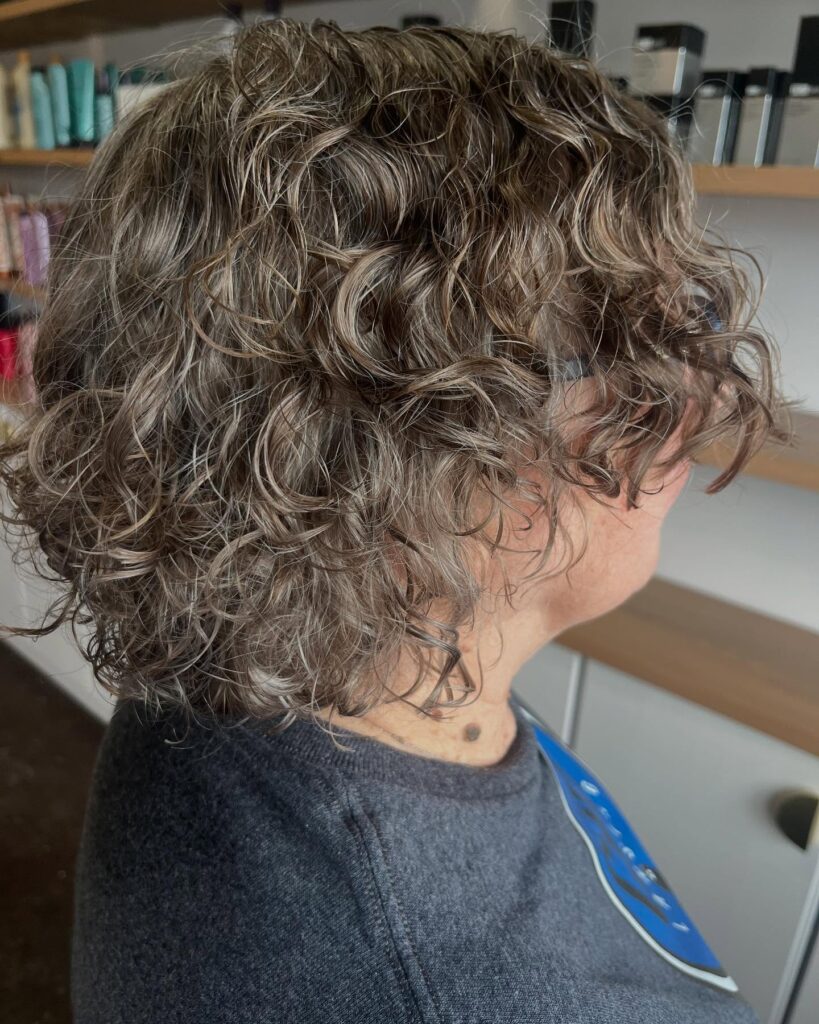 Ash brown layered curly bob with loose soft coils and dimensional texture.