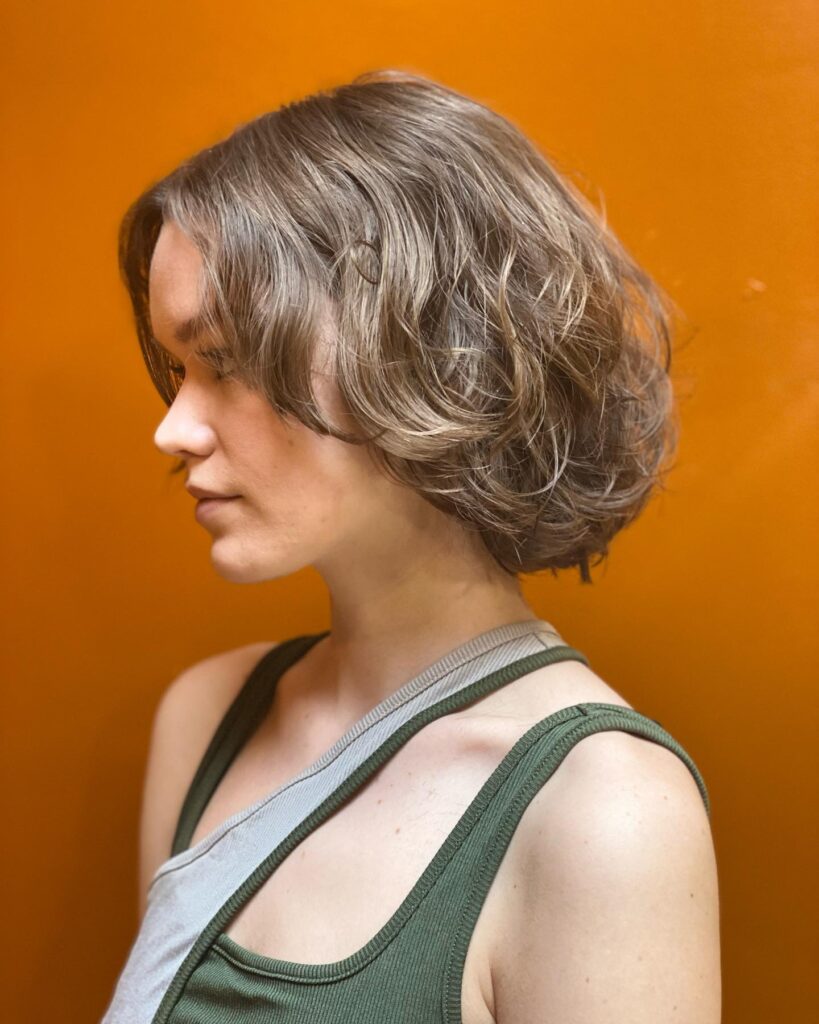 A chin-length layered bob with soft feathered waves and ash brown color.
