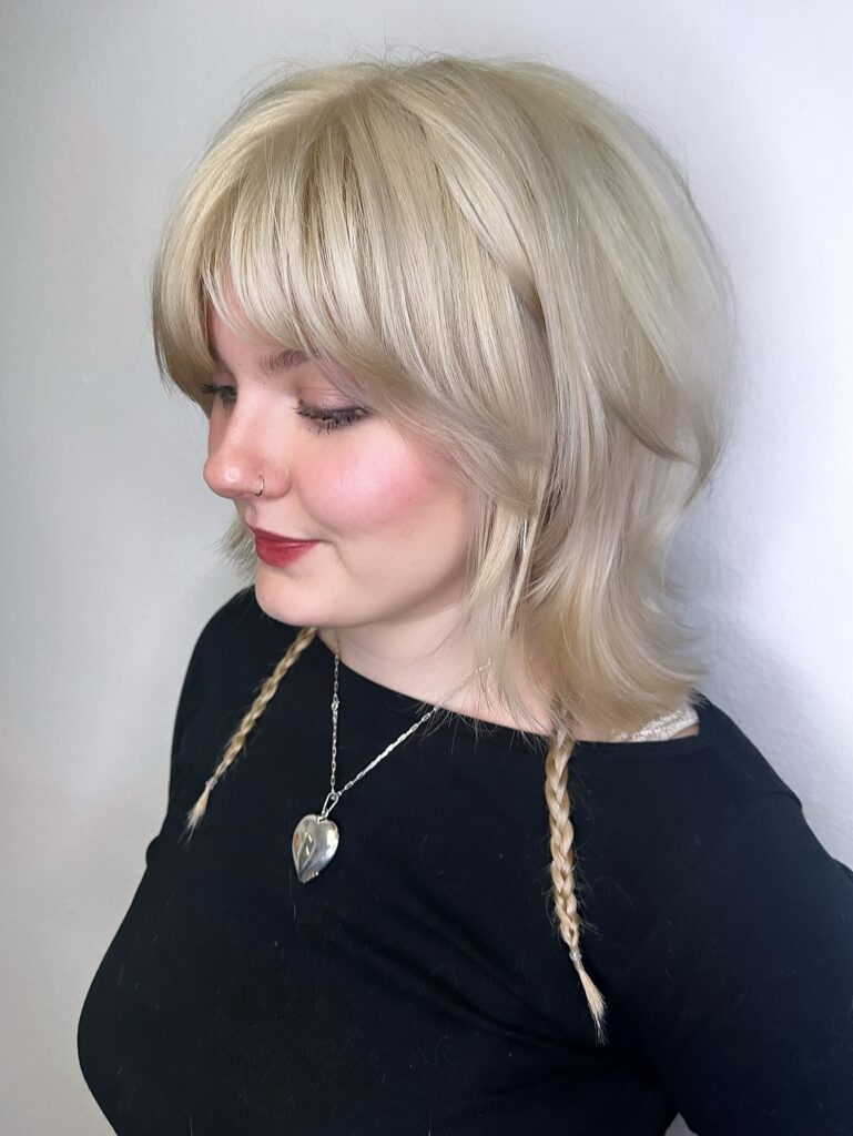 Soft shaggy blonde bob with feathered layers and curtain bangs.