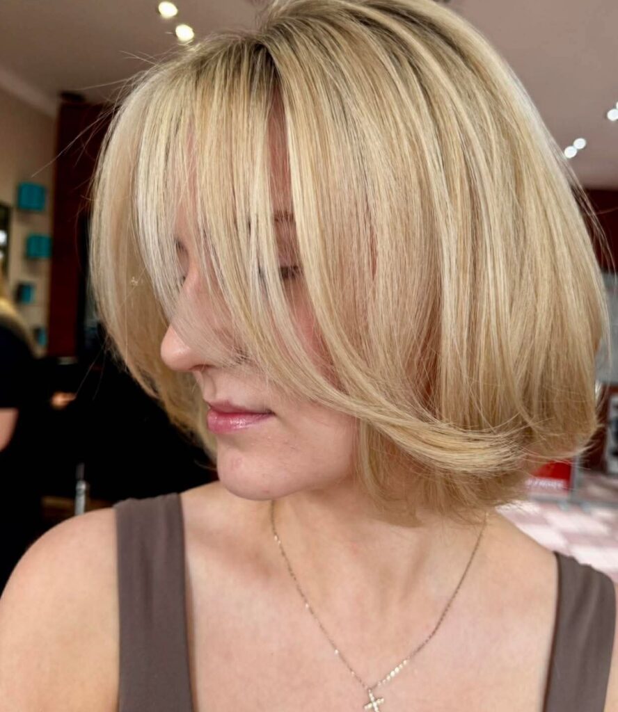 A creamy blonde bob with face-framing layers and long curtain bangs.