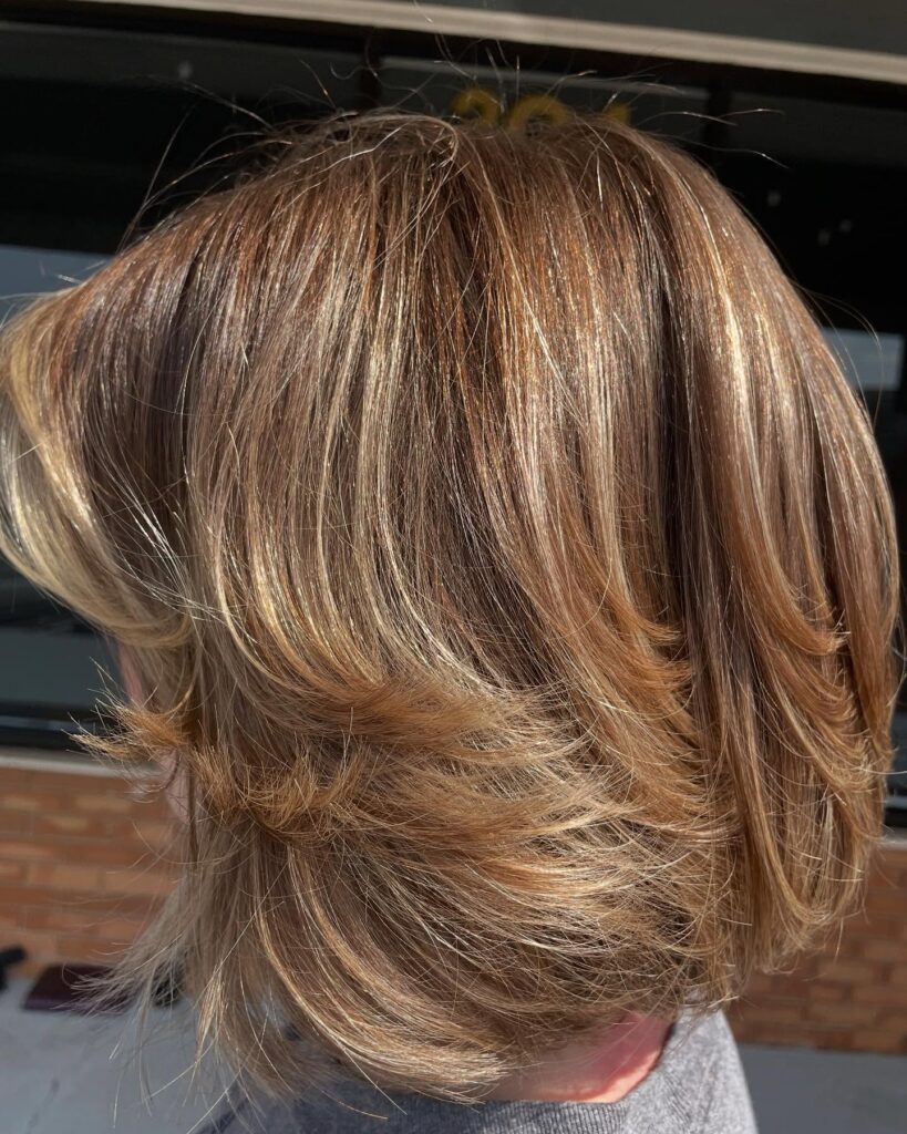 A feathered layered bob with warm honey highlights and soft flipped ends for extra movement and depth.