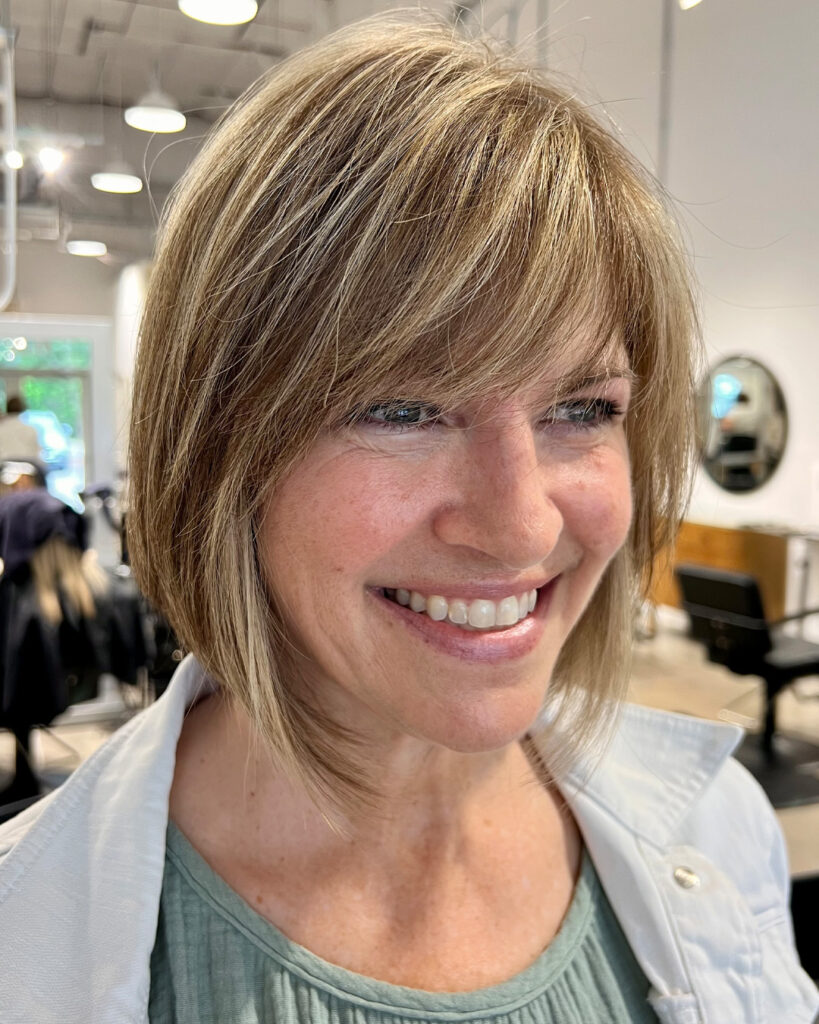 Layered bob with side-swept bangs and bright blonde highlights framing the face.