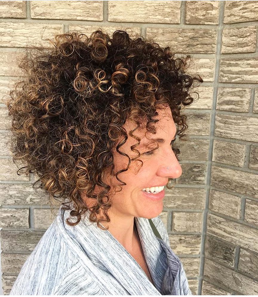 A brunette spiral curly bob with caramel highlights and rounded layers.