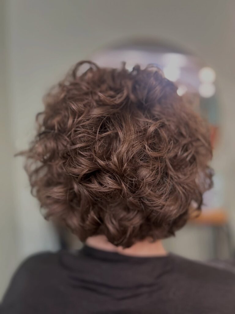 A rounded chocolate brown curly bob with soft layered curls and airy volume.