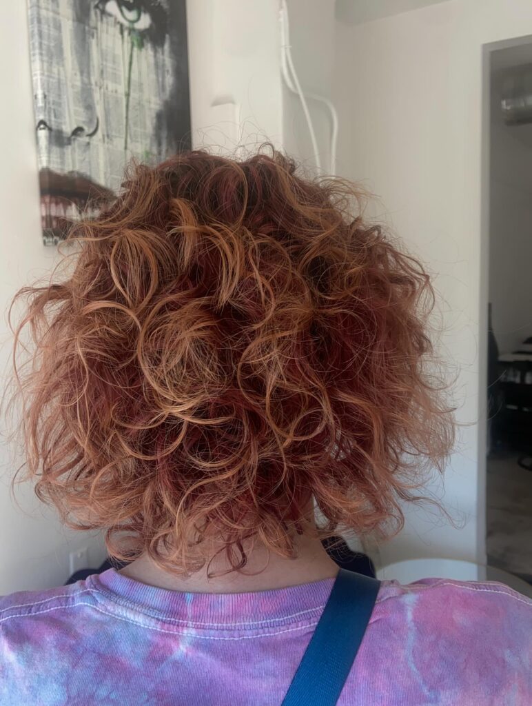 A tousled copper curly bob with layered ringlets and rounded volume.