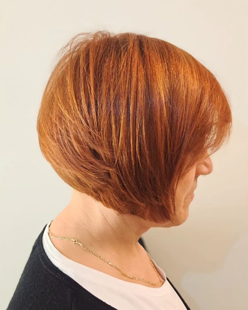 A woman in profile wearing a straight inverted bob in a rich copper shade with golden highlights.