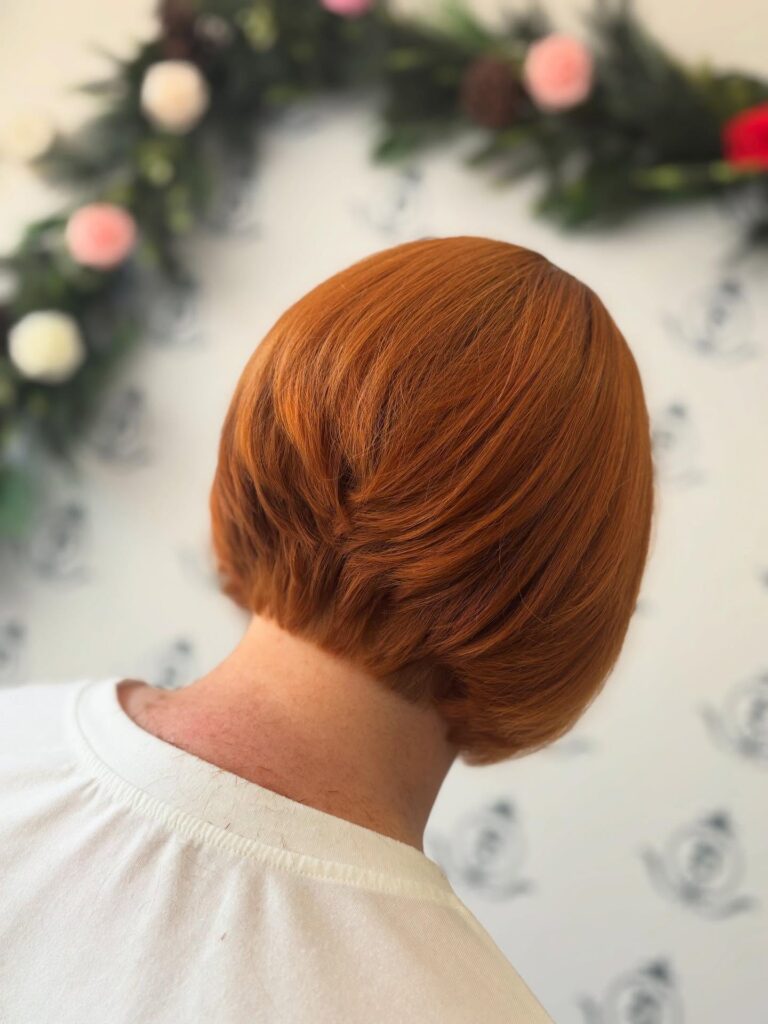 A rear view of a woman with a sleek, stacked bob in a bright pumpkin-copper color.