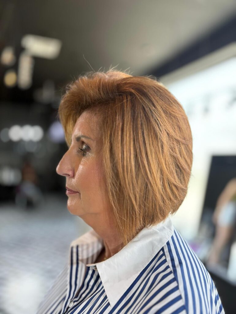 A woman in profile wearing a voluminous layered bob in a warm caramel copper shade with a side-swept fringe.