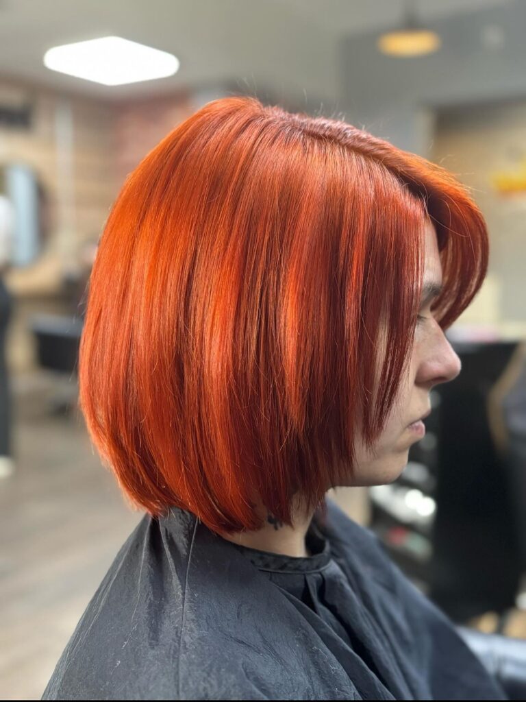 A woman in profile wearing a straight chin-length bob in a very bright and saturated electric copper color.