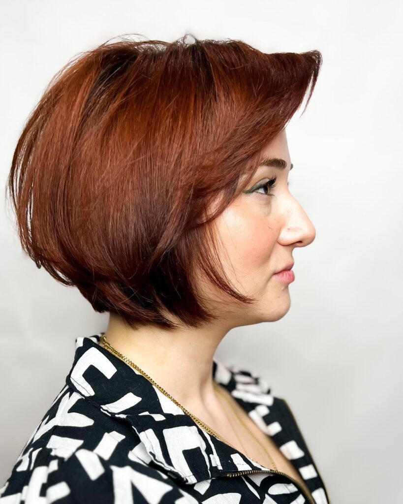 A woman in profile wearing a graduated bob with a stacked back in a deep russet-copper color.