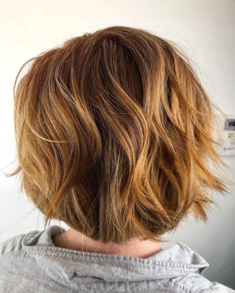 A rear view of a woman with a messy chin-length bob featuring soft waves and a caramel-copper color.