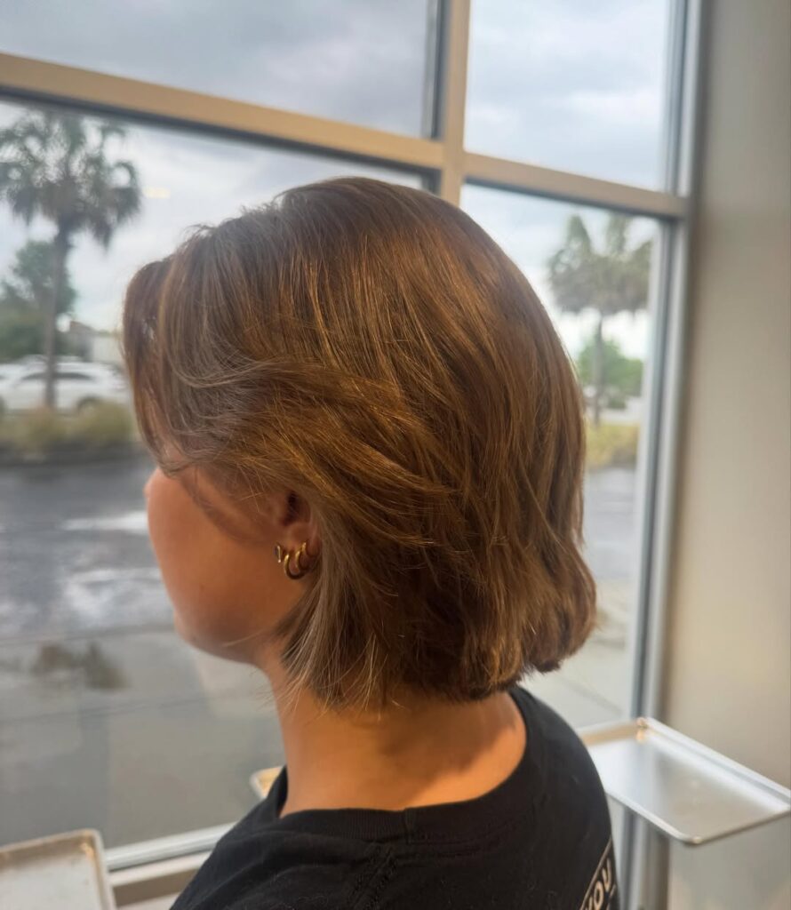 Warm auburn layered bob with side-swept curtain bangs and softly textured ends.