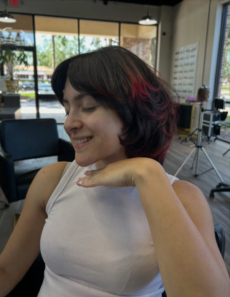 Short dark layered bob with wispy curtain bangs and cherry red highlights.