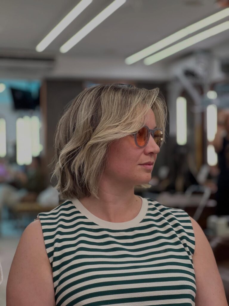 Sandy blonde layered bob with curtain bangs and soft wavy texture.