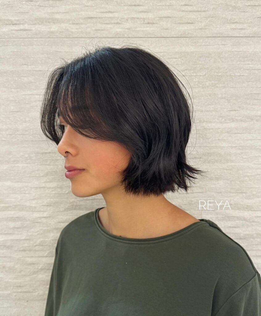Short textured dark bob with wispy curtain bangs and flipped layered ends.