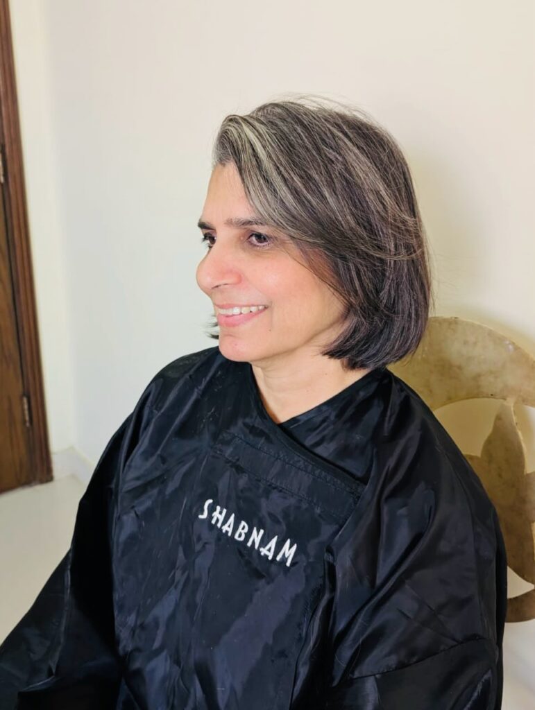 Salt and pepper layered bob with side-parted curtain bangs and soft rounded layers.