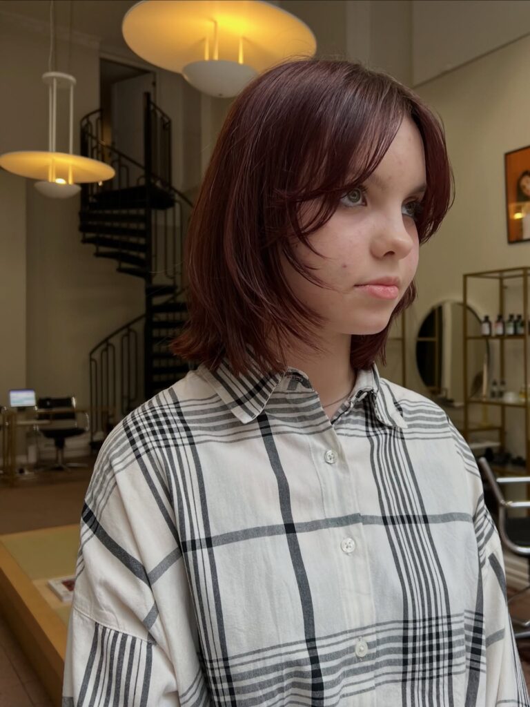 Burgundy layered bob with wispy curtain bangs and feathered ends.