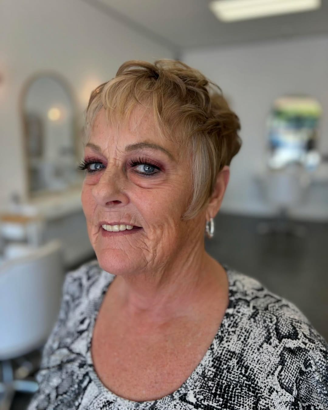 Short textured blonde pixie cut with soft layers, wispy bangs, and a neatly tapered nape that creates a light, modern style with natural volume.