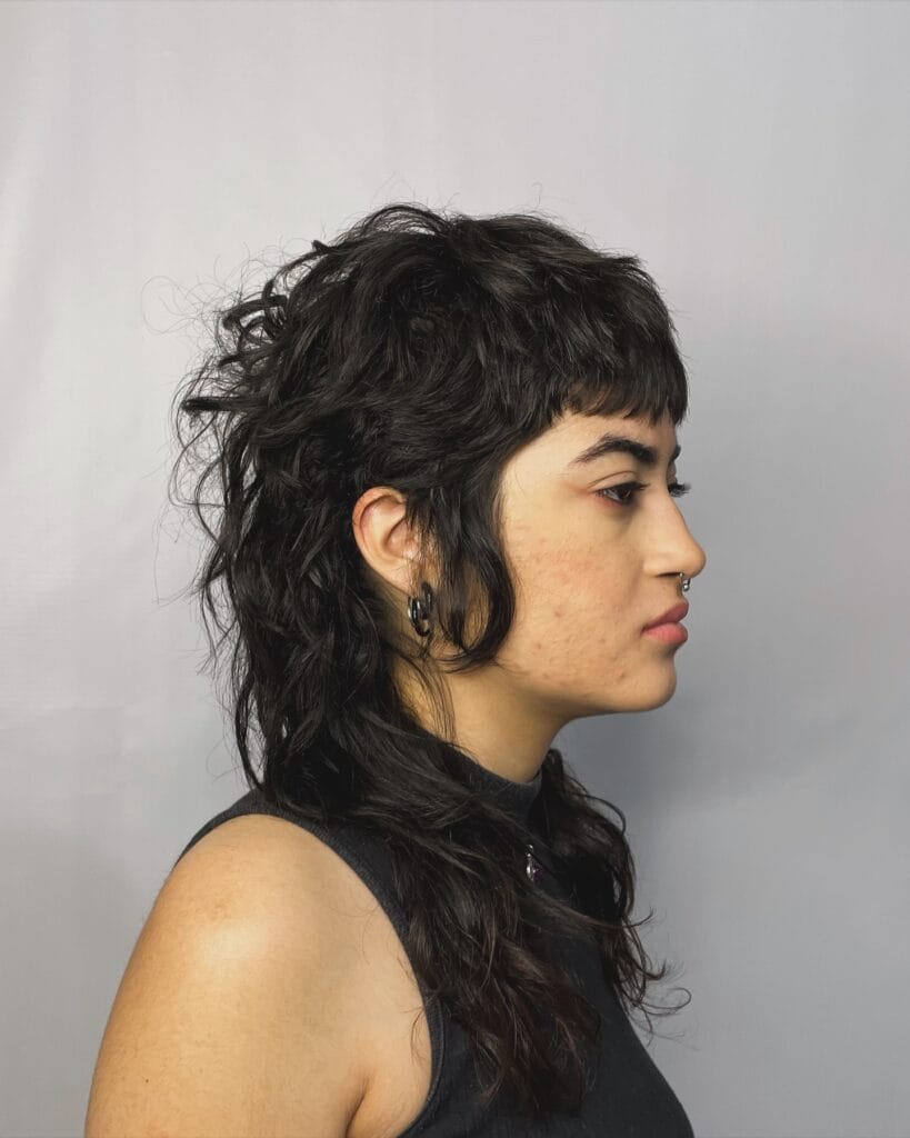 A woman with a long dark shaggy mullet featuring a piecey fringe and wavy layers.