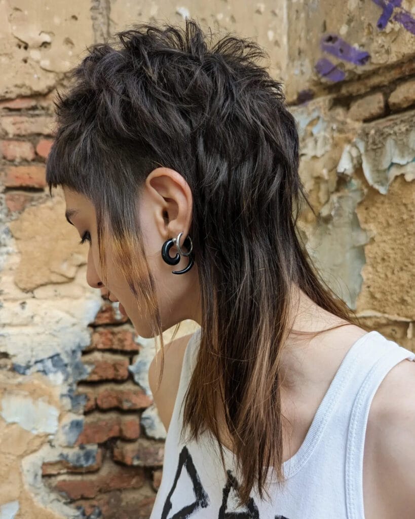 A woman with a dark brunette shaggy wolf-cut mullet featuring long straight layers and a textured crown.