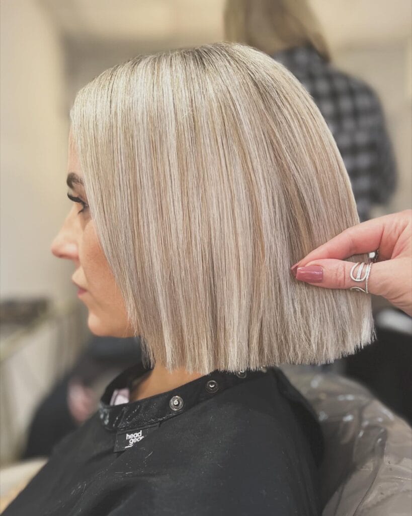 A side profile view of a woman with a sleek, one-length, sharp, blunt bob haircut in an ice-blonde hair color.