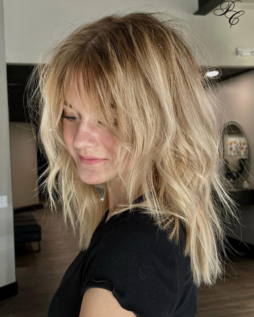 A woman with medium-length messy honey-blonde shaggy hair and wispy bangs.