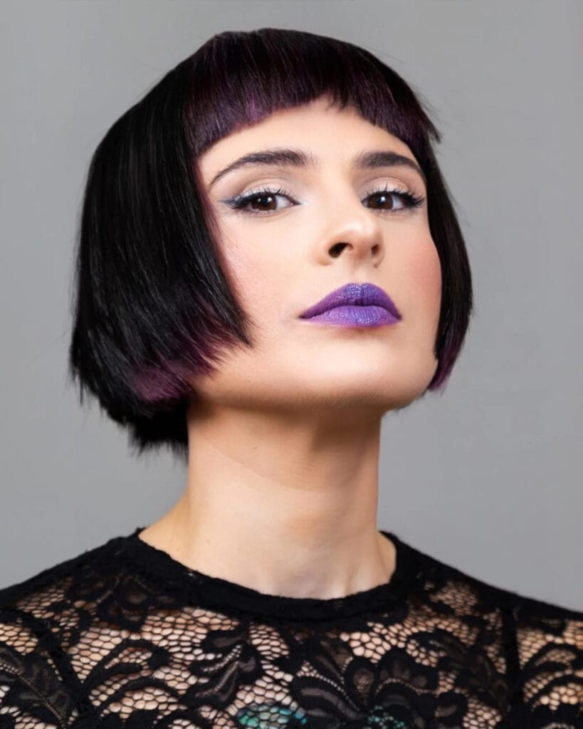 A woman with a very short, sleek black bob haircut featuring short blunt bangs and purple highlights on the tips.