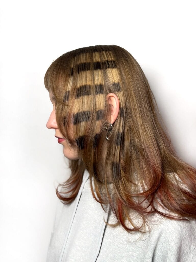 A woman with medium-length blonde hair featuring bold horizontal black stripes and face-framing layers.