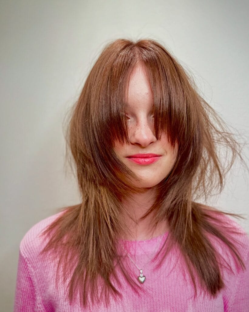 A woman with a medium-length copper wolf cut featuring a long fringe and shaggy layers.