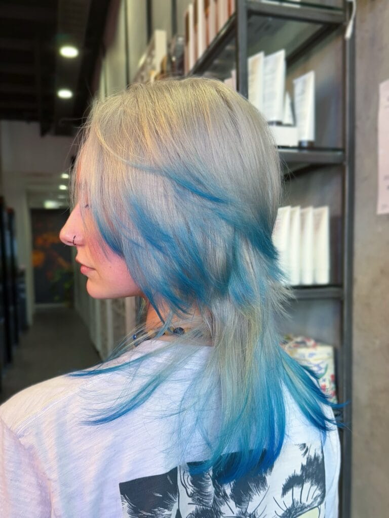A woman with a medium-length silver mullet featuring bright blue dyed layers and textured ends.