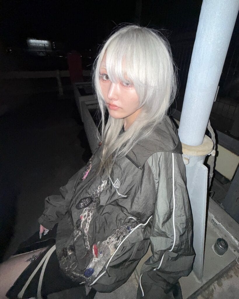 A woman with medium-length platinum white hair featuring a thick fringe and soft face-framing layers.