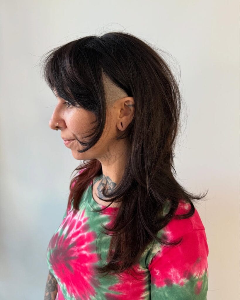 A woman with medium-length dark brown hair featuring layered ends and a shaved side undercut.