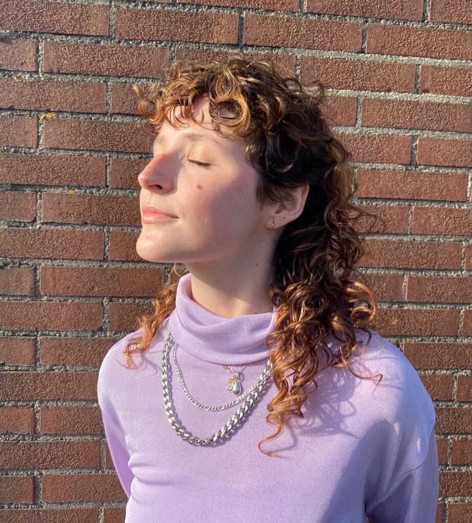 A woman with medium-length curly brown hair featuring golden highlights and a curly fringe.