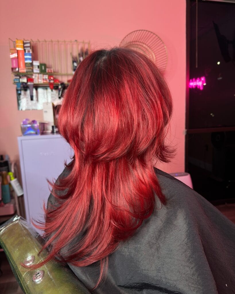 A woman with a medium-length fiery red layered shag haircut is shown from the back.